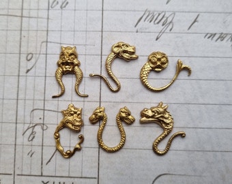May include: Six gold-toned metal dragon head charms with intricate details. The charms are in various poses, some with open mouths and others with closed mouths. The charms are perfect for adding a touch of fantasy to jewelry or crafts.