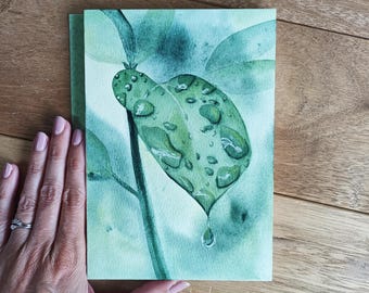 May include: Watercolor painting of a green leaf with water droplets. The leaf is the focal point, with a single drop of water falling from the tip. The background is a soft, muted green. The painting is on a rectangular piece of paper.