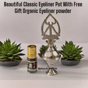 Op de afbeelding: Een zilveren metalen eyelinerpot met een decoratief deksel, een klein glazen flesje met zwarte eyeliner en de tekst "Mystique Art Enterprise".