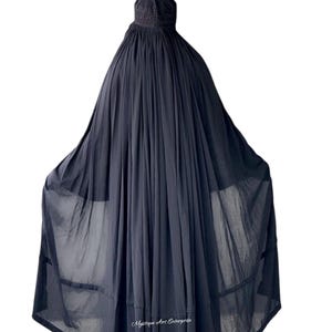以下が含まれることがあります： 頭を覆う黒色のロングドレス。生地は軽く、半透明で、縦のプリーツがドレープ効果を生み出しています。全身を覆うようにデザインされています。「Mystique Art Enterprise」の文字が見えます。