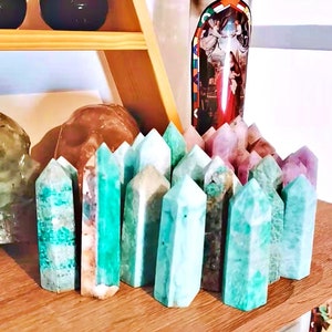 May include: A collection of green, blue, and purple crystal points arranged on a wooden shelf. The crystals are in various sizes and shapes, and some have a natural, rough texture.