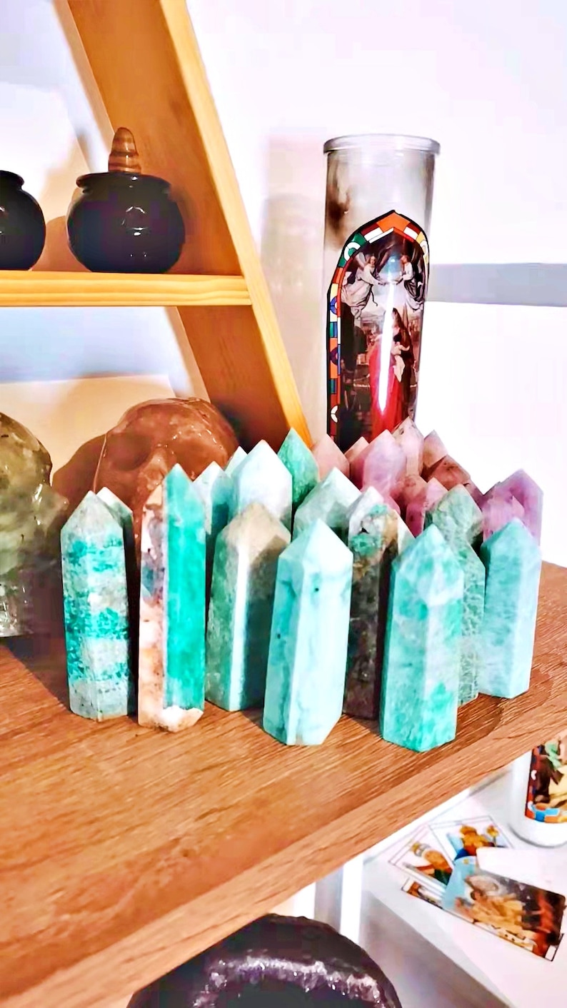 May include: A collection of green, blue, and purple crystal points arranged on a wooden shelf. The crystals are in various sizes and shapes, and some have a natural, rough texture.