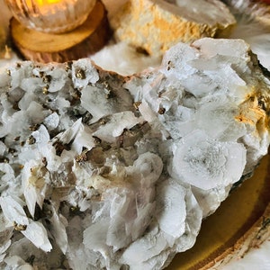 May include: A cluster of white calcite crystals with a layer of gold pyrite crystals. The calcite crystals are translucent and have a layered, flaky appearance. The pyrite crystals are small and scattered throughout the calcite.