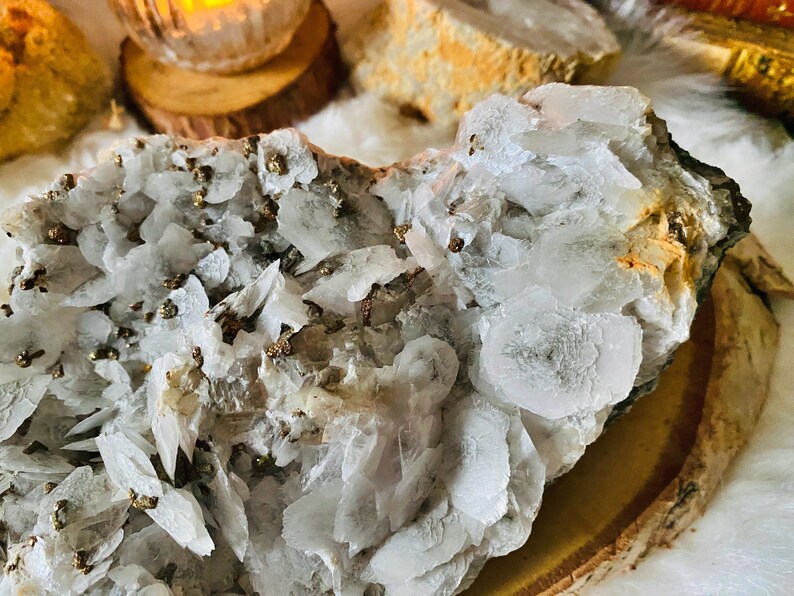May include: A cluster of white calcite crystals with a layer of gold pyrite crystals. The calcite crystals are translucent and have a layered, flaky appearance. The pyrite crystals are small and scattered throughout the calcite.