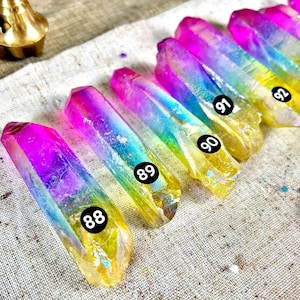 Peut inclure: Gros plan sur dix pointes de cristal arc-en-ciel irisées avec des pointes dorées. Chaque pointe est numérotée avec un autocollant noir, de 88 à 93. Les cristaux sont disposés en rangée sur un fond de tissu blanc.