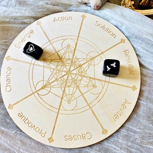 May include: A wooden circular game board with a geometric design in the center. The board has eight points around the edge, each with a word written in French. Two black dice with white symbols are on the board.