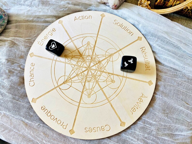 May include: A wooden circular game board with a geometric design in the center. The board has eight points around the edge, each with a word written in French. Two black dice with white symbols are on the board.