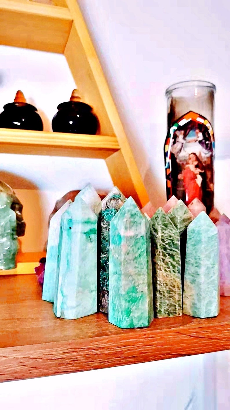 May include: A collection of green, pointed, polished, crystal stones, also known as green aventurine, arranged on a wooden shelf.