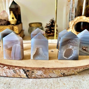 Peut inclure: Cinq petites tours de cristal d'agate grises et brunes avec une finition naturelle et drusique, disposées sur une tranche de bois. Les tours mesurent environ 5 cm de haut.