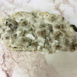 May include: A cluster of white and gray mica crystals with small, reddish-brown inclusions. The crystals are arranged in a rough, irregular shape.