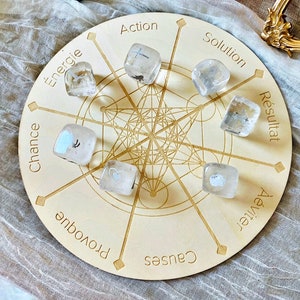 May include: A wooden circular board with a grid pattern and the words "Action", "Solution", "Resultat", "Chance", "Provoque", "Causes", "Avenir", "Energie" printed around the edge. There are eight clear quartz crystals with different symbols inside, placed on the board.