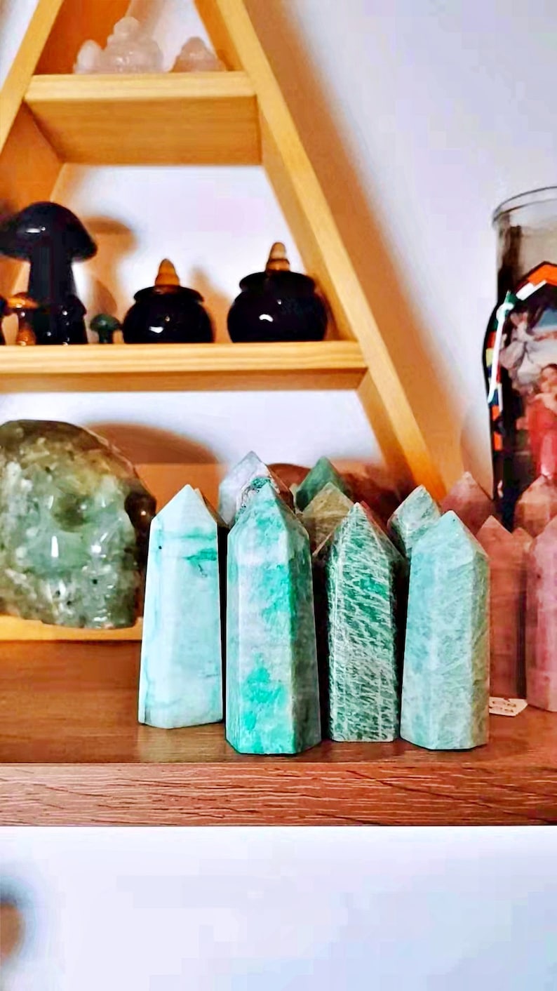 May include: A collection of green and white polished crystal points, also known as green aventurine, arranged on a wooden shelf.