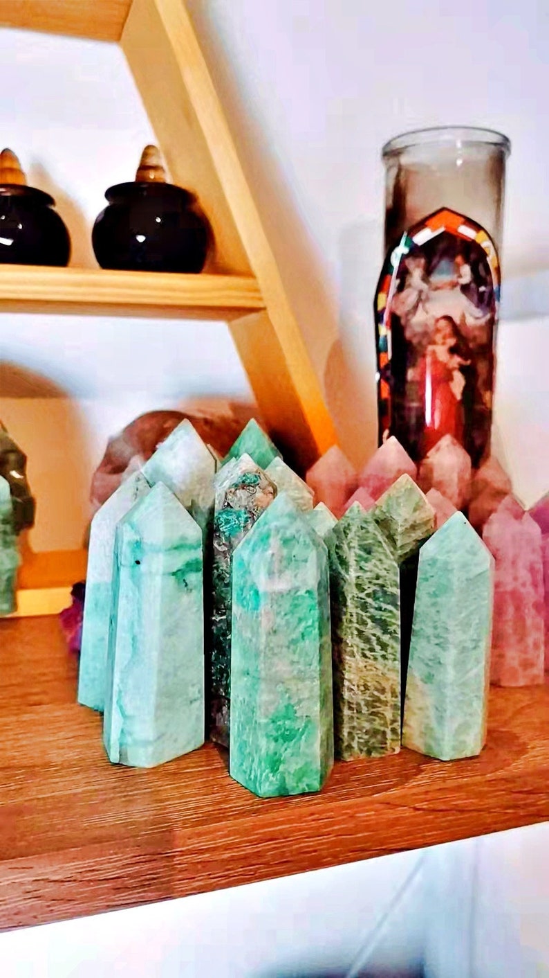May include: A collection of green, pink, and white crystal points arranged in a row on a wooden surface. The crystals are all pointed and have a natural, rough texture.