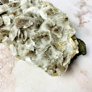 May include: A cluster of white, translucent crystals with small, brown, metallic inclusions. The crystals are arranged in a layered formation, creating a unique and interesting texture.