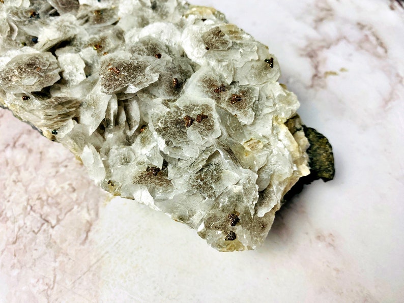 May include: A cluster of white, translucent crystals with small, brown, metallic inclusions. The crystals are arranged in a layered formation, creating a unique and interesting texture.