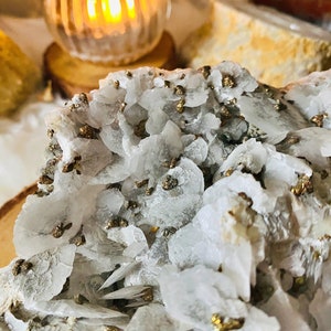 May include: Close-up of a white crystal cluster with gold pyrite inclusions. The crystal is rough and has a natural, organic shape.