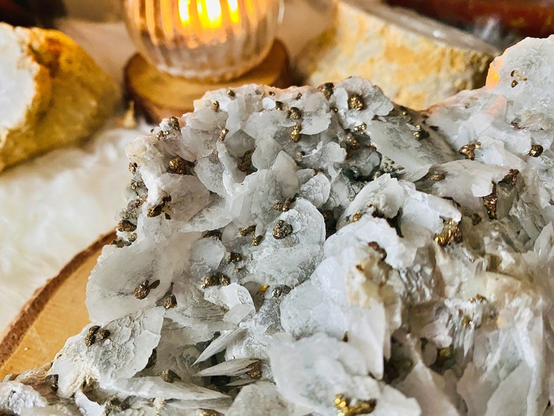 May include: Close-up of a white crystal cluster with gold pyrite inclusions. The crystal is rough and has a natural, organic shape.