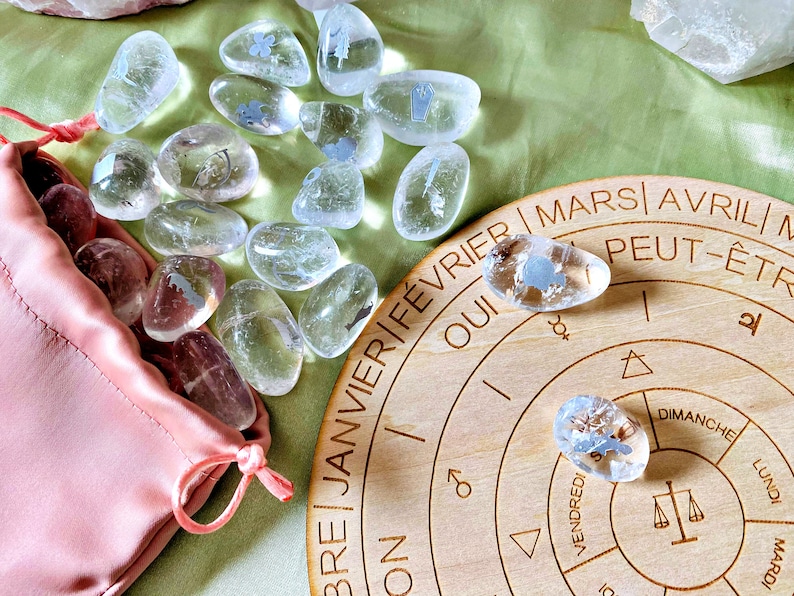 May include: A wooden circular board with a calendar design featuring French months and days of the week. The board is surrounded by clear quartz crystals with etched symbols. The crystals are in a pink satin bag.