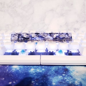 May include: A white mechanical keyboard with a black and white resin keyboard keycap set. The keycaps have a marbled design with black and white swirls. The keyboard is lit up with blue LEDs.