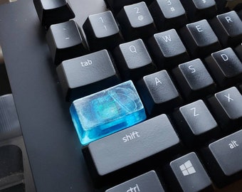 May include: A close-up of a black keyboard with a blue and clear keycap. The keycap is labeled "shift".