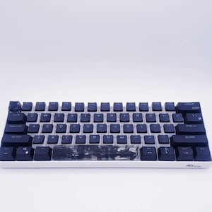 May include: A black and white mechanical keyboard with a black and white marble design on the space bar. The keyboard has a white frame and black keys with white lettering. The keys are labeled with the standard QWERTY layout. The keyboard has a black and white logo on the bottom right corner.