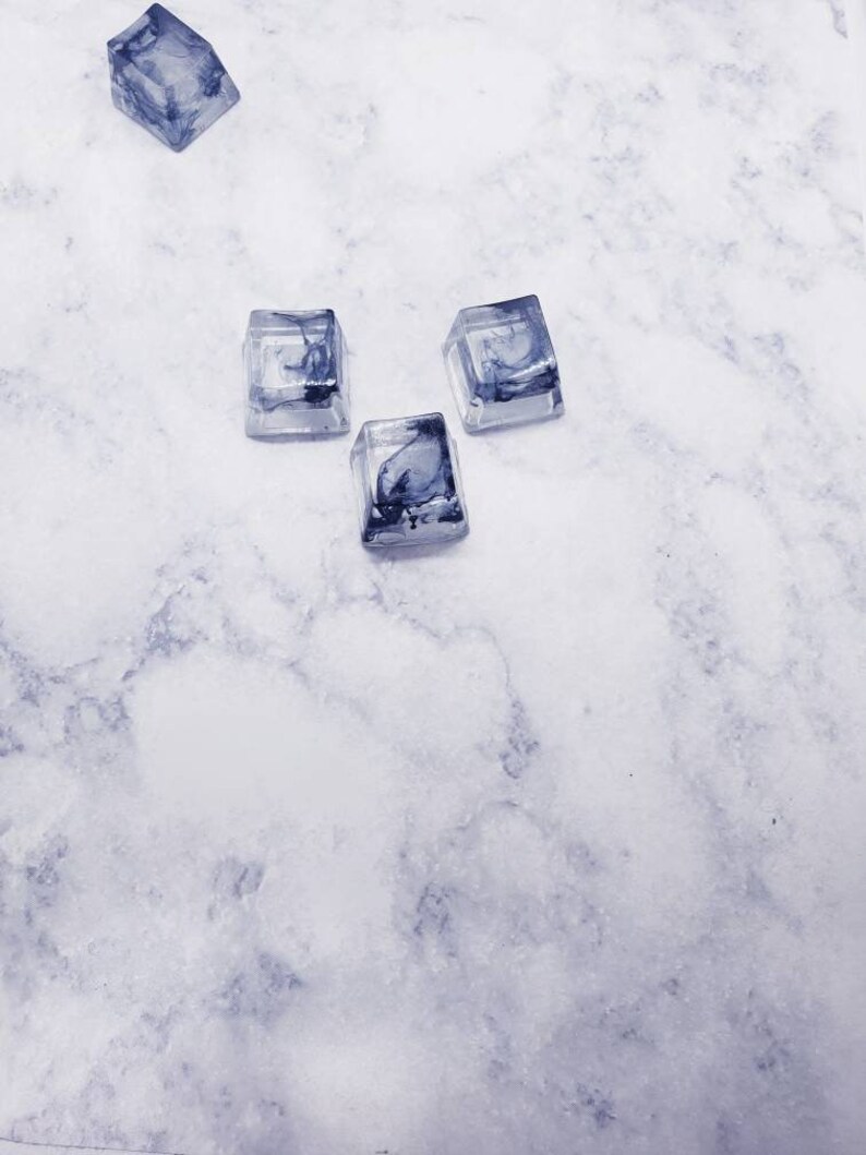 May include: Four clear resin keycaps with a marbled black and white design. The keycaps are arranged in a triangular shape on a white marble surface.