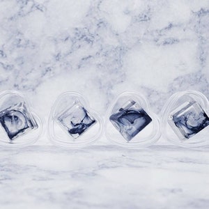 May include: Four clear heart-shaped containers with a black and white marbled design inside each one.