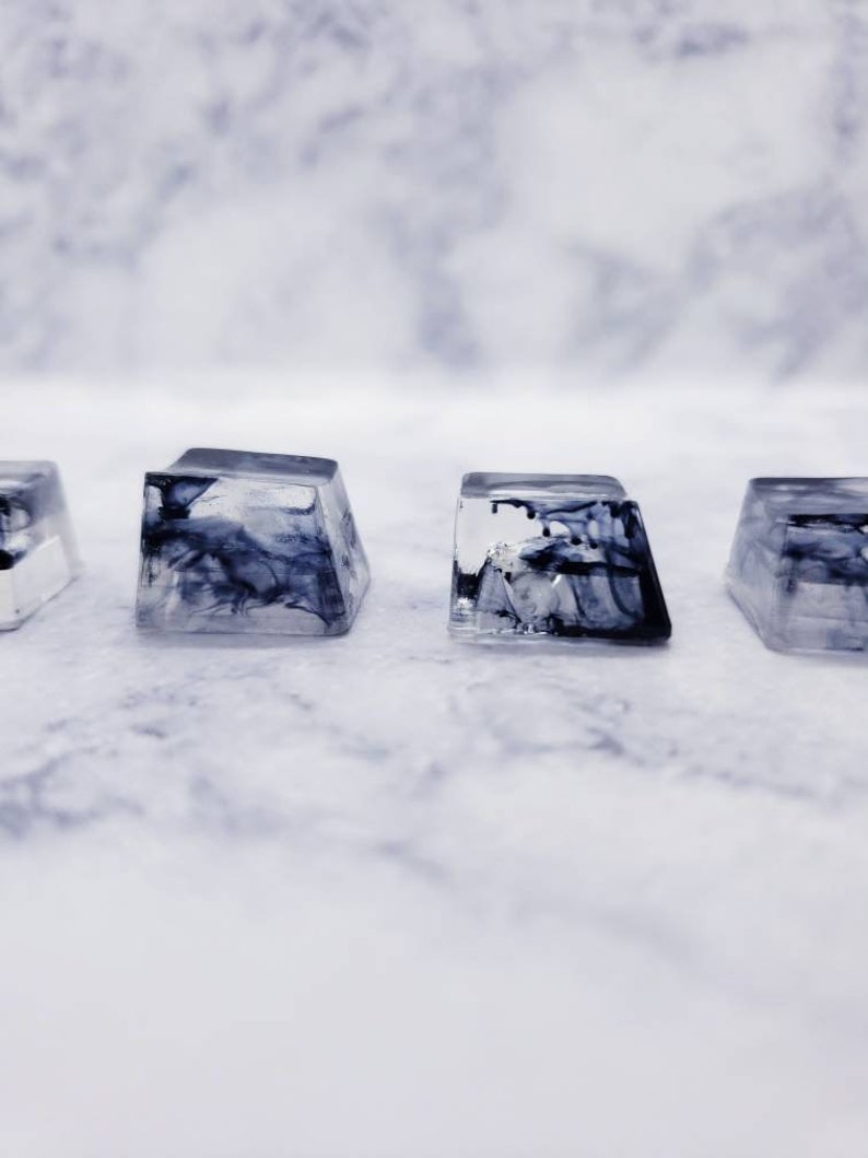 May include: Four clear resin keycaps with black and white marbled designs. The keycaps are square and have a slightly rounded top.