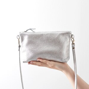 silver leather crossbody bag being held infront of a white background