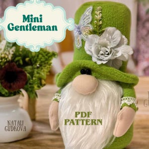 Puede incluir: Una muñeca de gnomo verde hecha a mano con barba blanca, nariz rosa y sombrero verde adornado con una flor blanca y una mariposa. Los textos "Mini Gentleman" y "PDF PATTERN" son visibles. La muñeca es parte de un proyecto de manualidades.