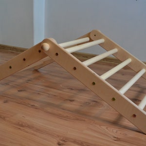 Op de afbeelding: Een houten klimlat met een driehoekig frame. De ladder heeft vijf sporten en is gemaakt van natuurlijk hout.