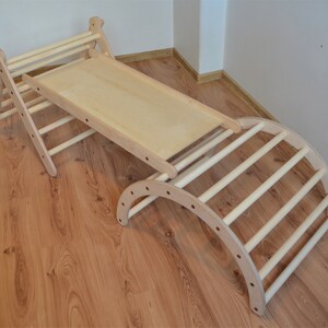 Op de afbeelding: Houten klimparadijs met een glijbaan en een gebogen ladder. Het frame is gemaakt van natuurlijk hout en heeft een lichtbruine afwerking.