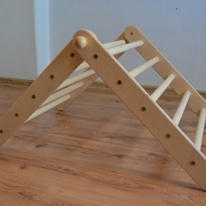 Op de afbeelding: Een driehoekig houten klimplatform met afgeronde randen en meerdere sporten. Het platform is gemaakt van natuurlijk hout en heeft een lichtbruine kleur.