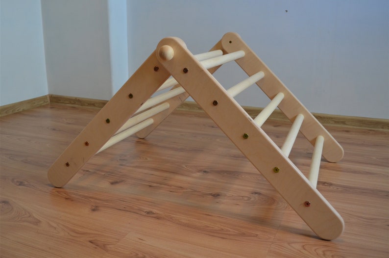 Op de afbeelding: Een driehoekig houten klimplatform met afgeronde randen en meerdere sporten. Het platform is gemaakt van natuurlijk hout en heeft een lichtbruine kleur.