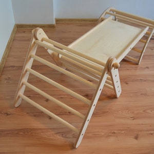 Op de afbeelding: Een houten klimplank met een glijbaan en een plat platform. Het frame is gemaakt van natuurlijk hout en heeft een lichtbruine kleur.