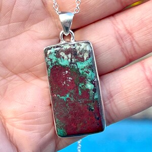 May include: A silver chain necklace with a rectangular pendant featuring a green and red stone with a marbled pattern.