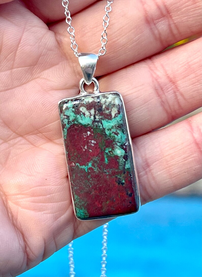 May include: A silver chain necklace with a rectangular pendant featuring a green and red stone with a marbled pattern.
