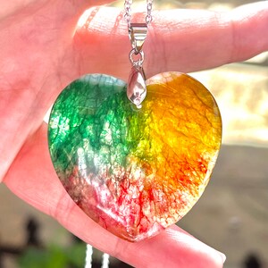 Puede incluir: Un collar con un colgante en forma de corazón con una cadena de plata. El colgante está hecho de ágata verde, amarilla y roja con un acabado transparente.