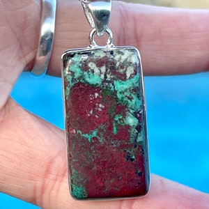 May include: A silver chain necklace with a rectangular pendant featuring a green and red gemstone. The pendant has a mottled pattern of green, red, and white.