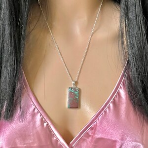 May include: A silver chain necklace with a rectangular pendant featuring a green and brown stone.