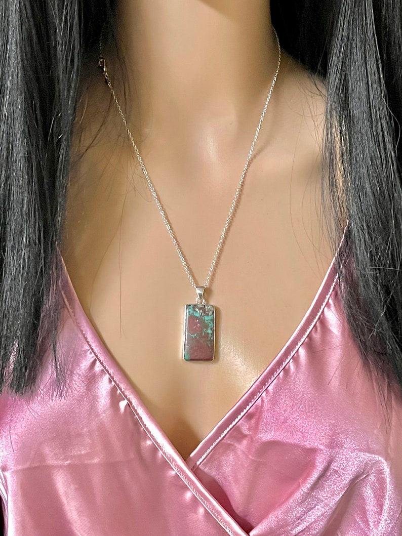 May include: A silver chain necklace with a rectangular pendant featuring a green and brown stone.