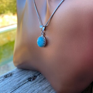 May include: A silver chain necklace with a light blue gemstone pendant. The pendant is oval shaped and has a silver border.
