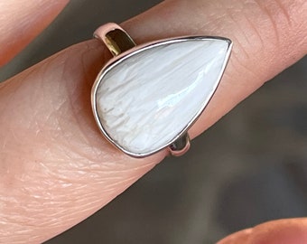 May include: A white teardrop-shaped ring with a silver band. The ring is made of natural materials and has a unique, organic look.