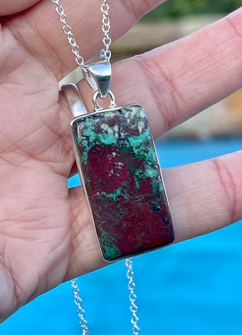 May include: A silver chain necklace with a rectangular pendant featuring a green, red, and white patterned stone.