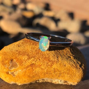May include: A silver ring with a light blue oval opal gemstone. The ring is sitting on a brown rock.