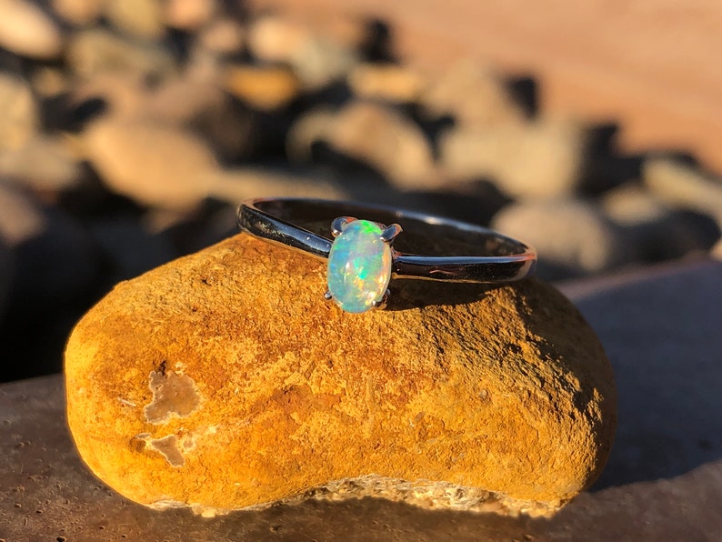 May include: A silver ring with a light blue oval opal gemstone. The ring is sitting on a brown rock.