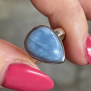 May include: A silver ring with a teardrop-shaped blue opal gemstone. The ring is on a finger.