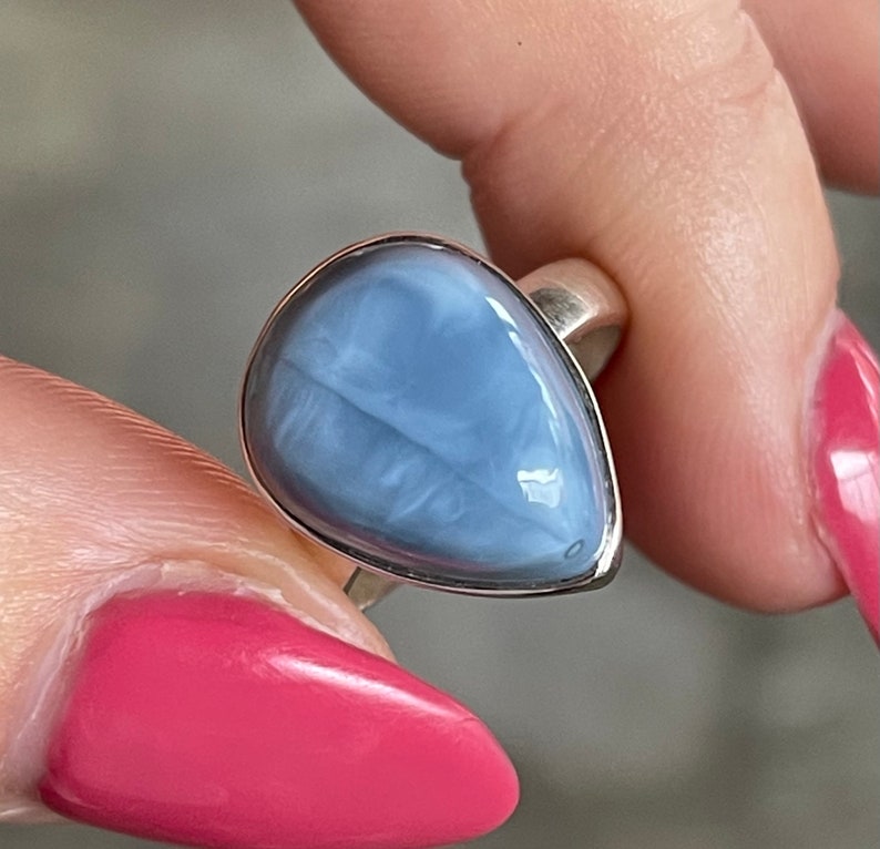 May include: A silver ring with a teardrop-shaped blue opal gemstone. The ring is on a finger.