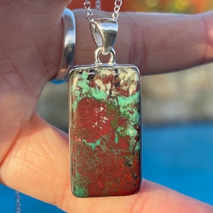 May include: A silver chain necklace with a rectangular pendant featuring a green, red, and white patterned stone.