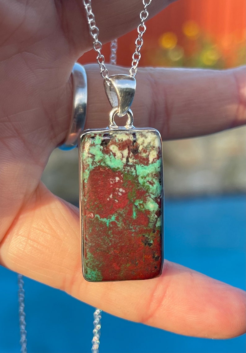 May include: A silver chain necklace with a rectangular pendant featuring a green, red, and white patterned stone.